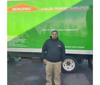male, black jacket posing front of green boxtruck